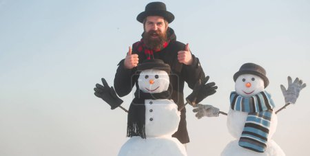 Foto de Feliz Navidad y feliz año nuevo. Hombre de nieve de invierno divertido en el juego de sombreros con muñeco de nieve al aire libre. Hombre con muñeco de nieve en invierno fondo al aire libre. Hombre de nieve para bandera de invierno - Imagen libre de derechos