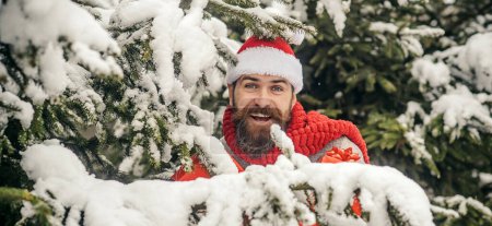 Téléchargez les photos : Père Noël portrait en plein air sur fond de neige d'hiver. Chapeau homme au Père Noël avec cadeaux de Noël en plein air. Fond hivernal enneigé. Père Noël en plein air dans les chutes de neige portant des cadeaux - en image libre de droit