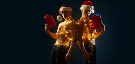 Photo for Sexy macho men with sexy muscular athletic strong body has bare torso and strong belly hold christmas or xmas present box on black studio background. Sexy muscular men - Royalty Free Image