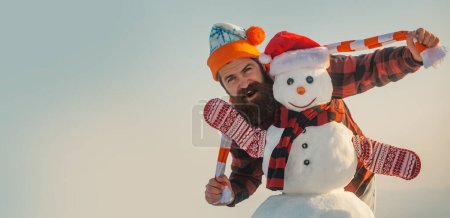 Téléchargez les photos : Jeune homme excité avec bonhomme de neige de Noël. Homme étonnant avec bonhomme de neige sur fond extérieur d'hiver. Bonhomme de neige pour bannière d'hiver. Noël et nouvelle année concept de neige, saison d'hiver - en image libre de droit