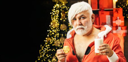 Photo for Santa fun. Portrait of Santa holding chocolate cookie and glass of milk. Old funny Santa enjoying gingerbread cake and milk - Royalty Free Image