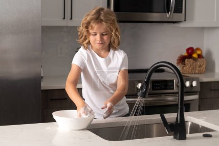 Photo for Child cleaning dishes with sponge. Cleaning supplies. Help clean-up. Housekeeping duties. Kid wash dishes. Kid boy washing dishes in the kitchen interior. Child helping his parents with housework - Royalty Free Image