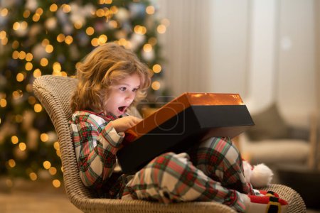 Foto de Sorpresa infantil abriendo regalos de magia navideña. Niño feliz cerca del árbol de Navidad en casa - Imagen libre de derechos