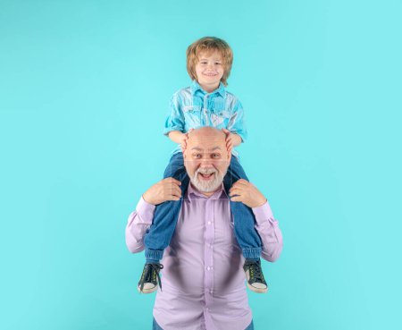 Téléchargez les photos : Jeune petit-fils et vieux grand-père piggyback avec drôle de visage isolé sur bleu en studio. Grand-père et mignon garçon avec un visage drôle - en image libre de droit