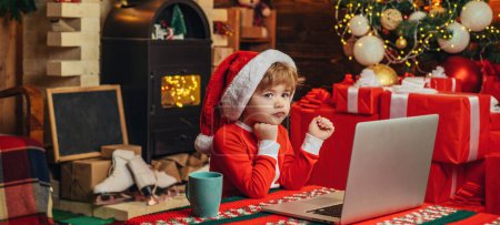 Foto de Niños inteligentes comprando regalos de Navidad. Niño de Navidad sueña cerca del ordenador portátil. Comprar compra regalos de Navidad en línea - Imagen libre de derechos