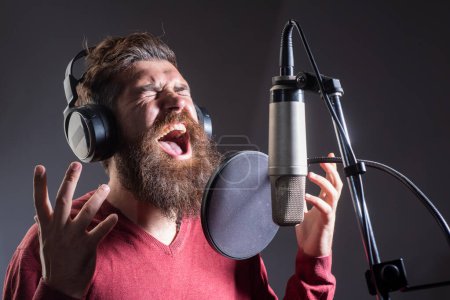Foto de Cantante con auriculares está interpretando una canción con un micrófono mientras graba en un estudio de música - Imagen libre de derechos