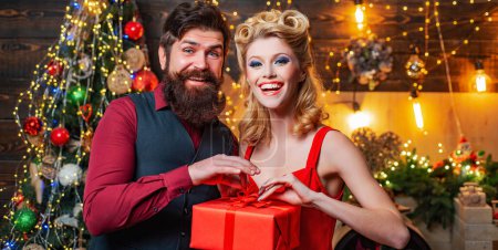 Téléchargez les photos : Couple en vêtements de Noël cadeau ouvert sur fond d'arbre de Noël. Cadeau émotions familiales - en image libre de droit