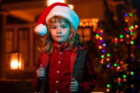 Photo for Child in backyard of night house decorated for Christmas Eve celebration. Child standing by illuminated night xmas house - Royalty Free Image