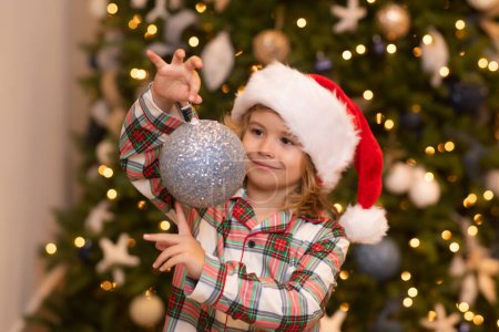 Foto de Feliz niño divertido en el sombrero de Santa cerca del árbol de Navidad. Navidad y Año Nuevo, concepto de vacaciones de invierno - Imagen libre de derechos
