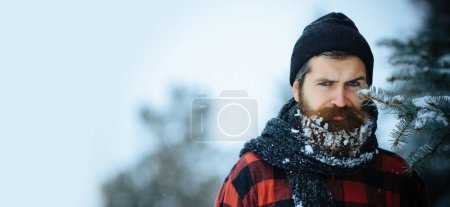 Close up portrait of serious bearded man in snow. Angry winter man with beard in snow on serious face. Brutal bearded man with snowy beard. Brutal hipster in in winter snowy background