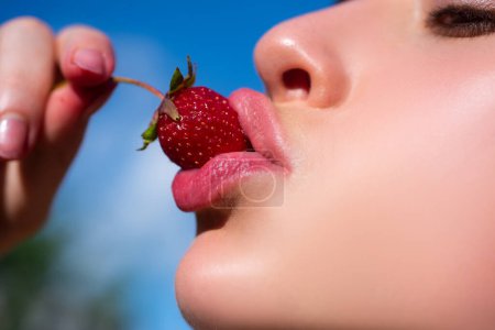 Fresa en los labios. Fresa roja en boca de mujer de cerca. Frutas sexys de verano. Hermosa chica, fresas en la boca