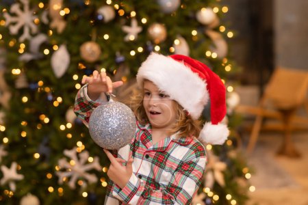 Téléchargez les photos : Joyeux Noël. Noël et bonnes vacances à la maison. Joyeux garçon mignon décoré arbre de Noël. Enfants avec boule de Noël et jouets près de l'arbre dans la chambre - en image libre de droit