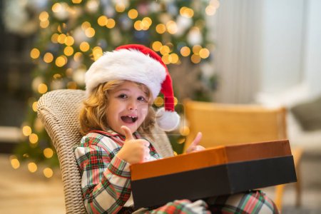 Téléchargez les photos : Surprise enfant ouvrant cadeaux magiques de Noël. Petit enfant excité ouvert avec boîte cadeau de Noël, célébrant Noël ou Nouvel An près de l'arbre de Noël à la maison - en image libre de droit