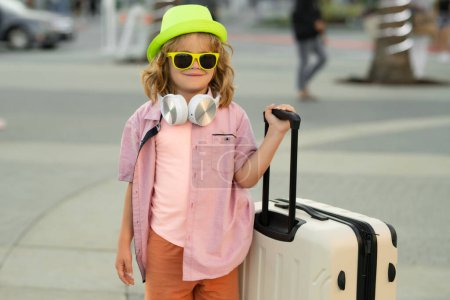 Foto de Niños viajando. Un niño con una maleta de vacaciones. Turista de vacaciones, concepto de viaje para niños. Lindo chico con maleta en el fondo de la calle de la ciudad - Imagen libre de derechos
