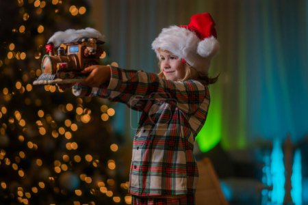 Téléchargez les photos : Le gamin s'amuse près du sapin de Noël la nuit. Joyeux Noël et bonne année. Enfant célébrant la veille de Noël - en image libre de droit