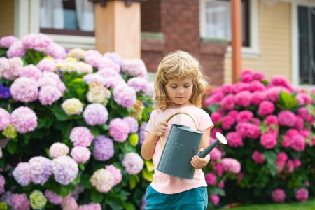 Téléchargez les photos : Petit garçon arrosant des fleurs et aide à prendre soin des plantes avec un arrosoir - en image libre de droit