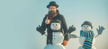 Foto de Hombre de nieve de invierno divertido en el juego de sombreros con muñeco de nieve al aire libre. Hombre con muñeco de nieve en invierno fondo al aire libre. Hombre de nieve para bandera de invierno - Imagen libre de derechos