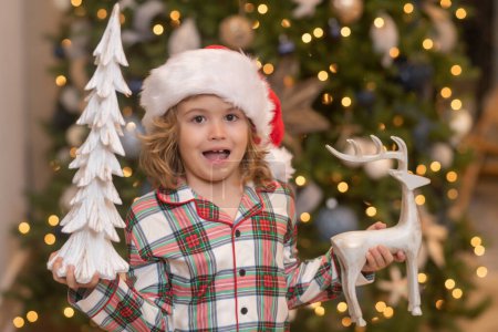 Téléchargez les photos : Joyeux Noël. Noël et bonnes vacances à la maison. Joyeux garçon mignon décoré arbre de Noël. Enfants avec boule de Noël et jouets près de l'arbre dans la chambre - en image libre de droit
