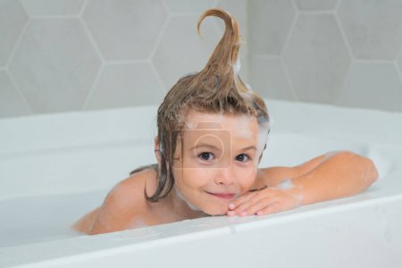 Téléchargez les photos : Shampooing pour enfants. Enfant s'amuser dans le bain avec des bulles. Joyeux enfant appréciant l'heure du bain. Petit garçon souriant dans le bain avec de la mousse de savon. Bains pour enfants dans un bain avec mousse - en image libre de droit