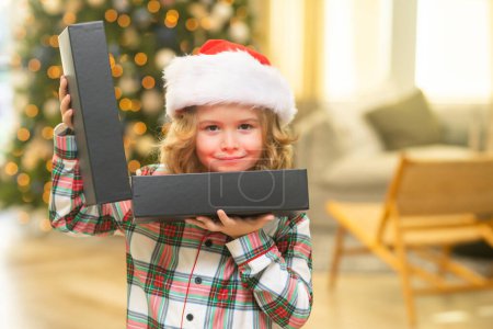 Foto de Sorpresa niño abriendo regalo de Navidad caja de regalo. Feliz niño divertido en el sombrero de Santa celebración de regalo de Navidad. Concepto de Navidad y Año Nuevo - Imagen libre de derechos