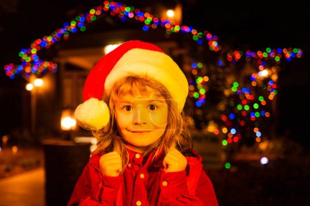 Téléchargez les photos : Petit enfant célébrant Noël ou Nouvel An près de la maison de Noël de nuit arrière-cour. Enfant sur la décoration de Noël devant une maison de nuit. Enfant debout près de la nuit illuminée maison de Noël - en image libre de droit