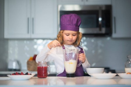 Foto de Niño con sombrero de chef y delantal. Niño haciendo sabroso delicioso. niño en sombrero de chef y un delantal cocinando en la cocina - Imagen libre de derechos