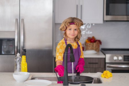 Foto de Adorable ayudante de limpieza infantil. Pequeño niño lindo barrer y limpiar los platos en la cocina - Imagen libre de derechos