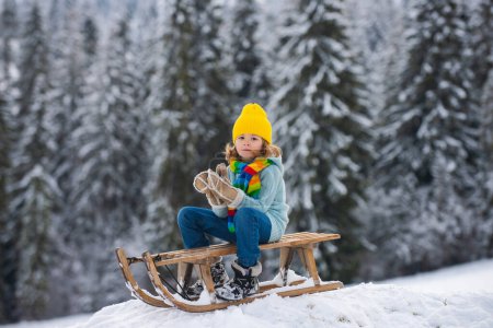 Téléchargez les photos : Garçon appréciant une promenade en traîneau, jouer avec la boule de neige. Enfant en traîneau. L'enfant joue dehors dans la neige. Hiver, vacances et Noël - en image libre de droit