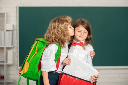 Téléchargez les photos : Amis d'école, câlins et baisers. Portrait de deux élèves heureux qui étudient en classe à l'école primaire - en image libre de droit