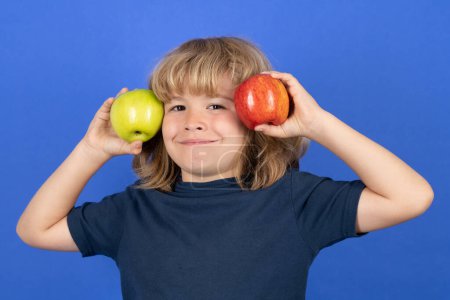 Téléchargez les photos : Un gamin qui choisit entre une pomme rouge et une pomme verte. Isolé sur fond bleu - en image libre de droit