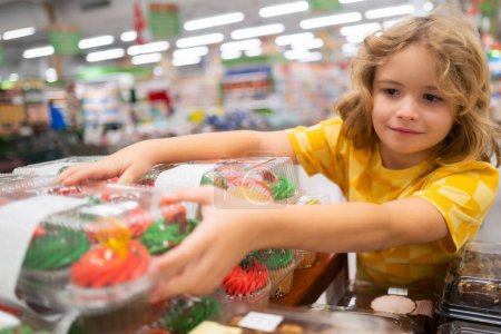 Téléchargez les photos : Un gamin qui choisit des gâteaux, muffin au cupcake. Shopping en supermarché ou épicerie. enfant acheter de la nourriture - en image libre de droit