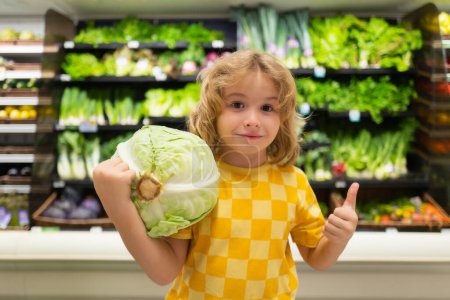 Foto de Niño con repollo. Niño en el supermercado de verduras. Pequeño niño eligiendo comida en la tienda o tienda de comestibles - Imagen libre de derechos