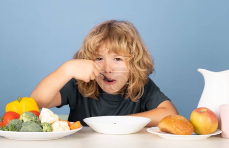 Téléchargez les photos : Un mignon petit garçon qui mange de la soupe pour le déjeuner. Soupe pour enfants - en image libre de droit