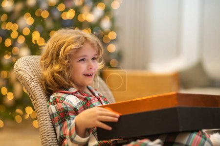 Foto de Feliz niño divertido en pijama de invierno cerca del árbol de Navidad por la mañana. Concepto de Navidad y Año Nuevo - Imagen libre de derechos