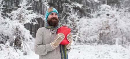 Téléchargez les photos : Homme heureux avec cadeau en hiver en plein air. Hipster homme avec chapeau tricoté et pull d'hiver s'amuser à l'extérieur. Guy visage heureux sur fond de nature enneigée d'hiver - en image libre de droit