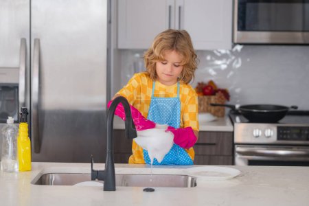Foto de Limpieza de casa. Lindo niño ayudando con el hogar, limpiando platos en la cocina. Adorable ayudante de limpieza infantil. Pequeño niño lindo barrer y limpiar los platos en la cocina - Imagen libre de derechos