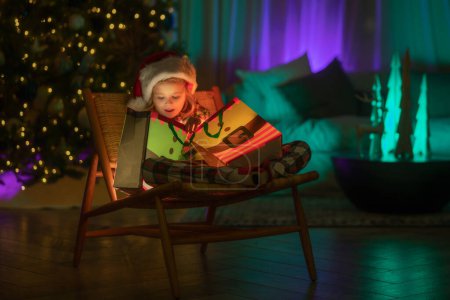 Foto de Niño regalo regalo abierto con luz mágica. Iluminación regalo bolsa. Feliz Navidad y Feliz Año Nuevo. Niño celebrando la Nochebuena - Imagen libre de derechos