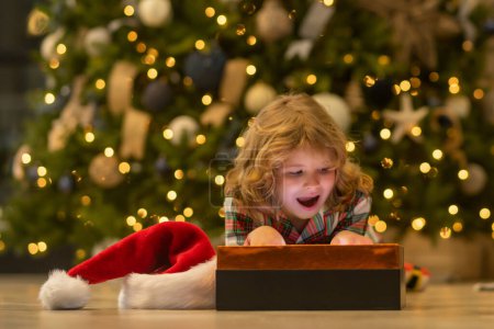 Foto de Sorpresa niño abriendo regalo de Navidad caja de regalo. Niño cerca del árbol de Navidad en casa - Imagen libre de derechos