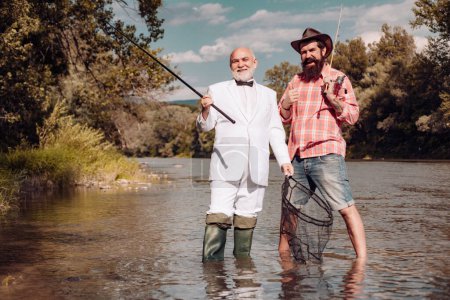 Téléchargez les photos : Pêcheur senior en costume et barbu homme occasionnel pêche avec canne à pêche - en image libre de droit