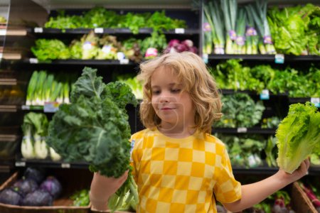 Téléchargez les photos : Enfant avec des légumes à la laitue. Enfant choisissant des fruits et légumes pendant les achats au supermarché de légumes - en image libre de droit
