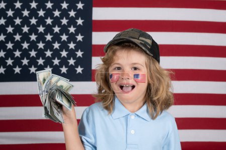 Téléchargez les photos : L'argent américain. Portrait d'enfant avec billets de banque. Enfant avec de l'argent. Les enfants apprennent la responsabilité financière de l'épargne. Drapeau américain sur la joue de l'enfant. Portrait d'enfant américain - en image libre de droit