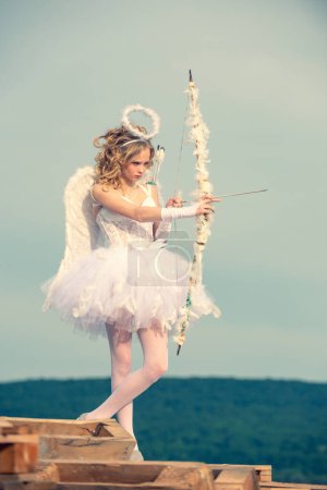 Photo for Valentines day cupid. A beautiful teen with blonde curly hair and a bow and arrow as cupid - Valentines Day. Portrait of little curly blond Angel girl. Lovely and cute youth. - Royalty Free Image