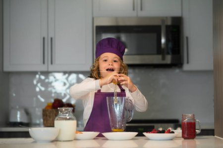 Foto de Cocinar en la cocina. Chef cocinero niño se divierten preparando un pastel en la cocina en casa. Niño en sombrero de chef y un delantal cocinando en la cocina - Imagen libre de derechos