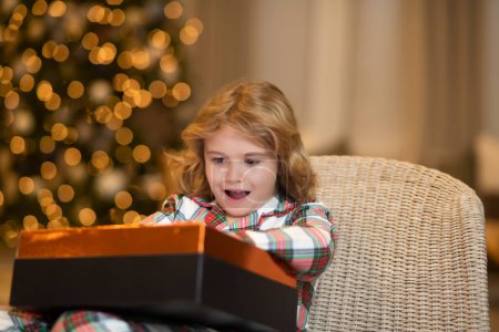 Téléchargez les photos : Petit enfant célébrant Noël ou Nouvel An près de l'arbre de Noël à la maison - en image libre de droit