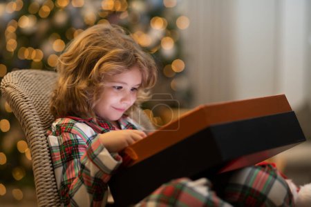 Foto de Sorpresa niño abriendo regalo de Navidad caja de regalo. Niño pequeño celebrando Navidad o Año Nuevo cerca del árbol de Navidad en casa - Imagen libre de derechos