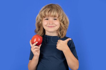 Téléchargez les photos : Une saine alimentation. Enfant souriant avec les pouces levés tenir pomme. Portrait de mignon garçon isolé sur fond de studio - en image libre de droit