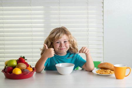 Photo for Schoolchild eating breakfast before school. Portrait of little teen child sit at desk at home kitchen have delicious tasty nutritious breakfast - Royalty Free Image