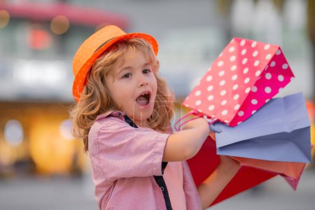 Photo for Excited kid in fashion clothes goes shopping. Amazed kid with shopping packages outdoor. Shopper child with shopping bag walking on street and carrying shopping bags - Royalty Free Image