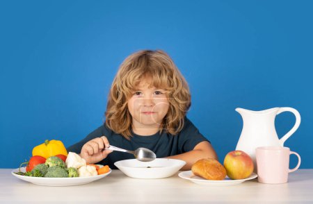 Téléchargez les photos : Un enfant qui mange de la soupe. Les enfants prennent le petit déjeuner. Portrait studio d'un petit garçon mangeant un repas de soupe ou un petit déjeuner déjeuner à table avec cuillère - en image libre de droit