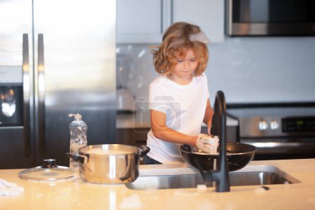 Foto de Los niños ayudan a lavar los platos en la cocina. Lavavajillas líquido con una esponja en el fregadero de la cocina - Imagen libre de derechos
